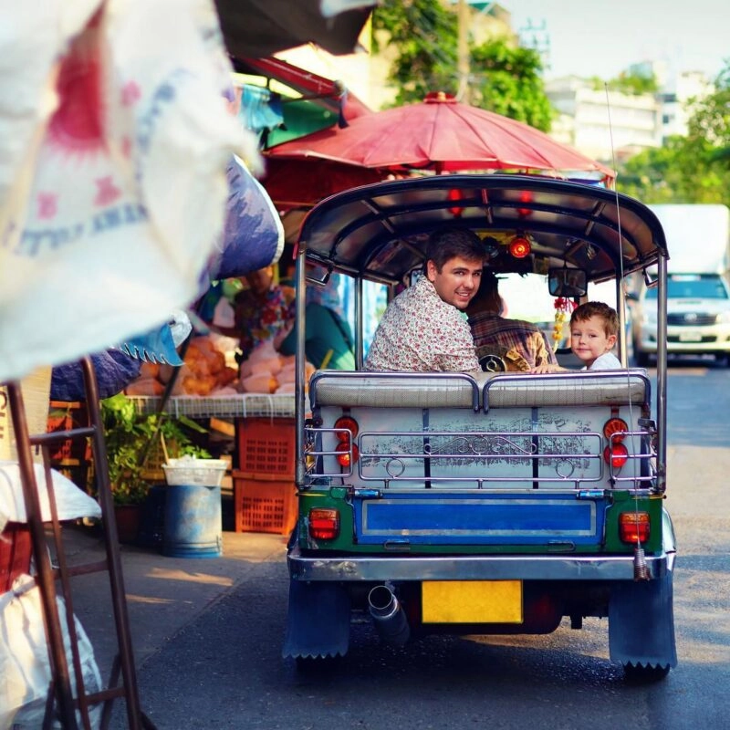 happy tourist family travel through the asian city on tuk-tuk