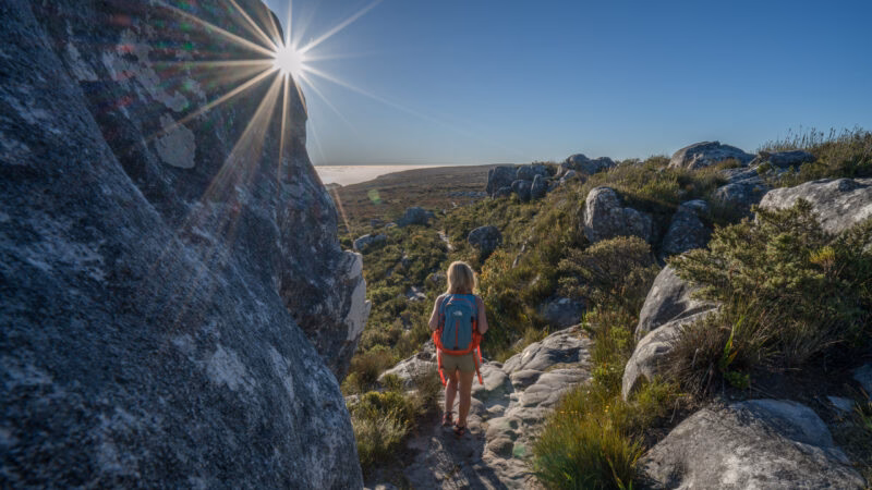 Hiker with a backpack on a rocky mountain trail with a bright sun star on luxury Cape Town holidays.