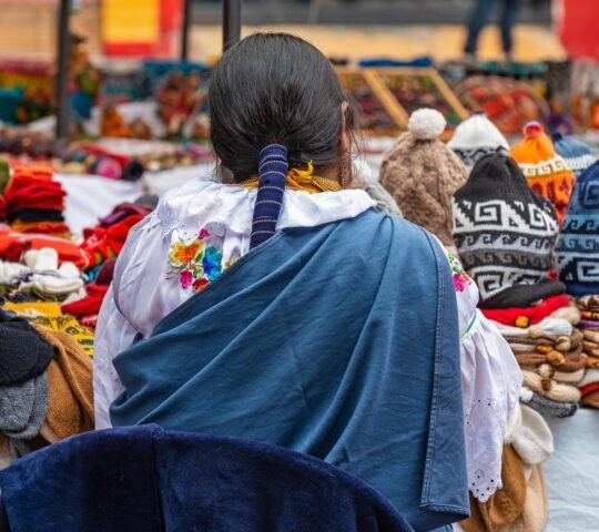 Indigenous women in traditional clothing and hairstyle by her market stall on the sunday art and craft market of Otavalo, North of Quito, Ecuador.