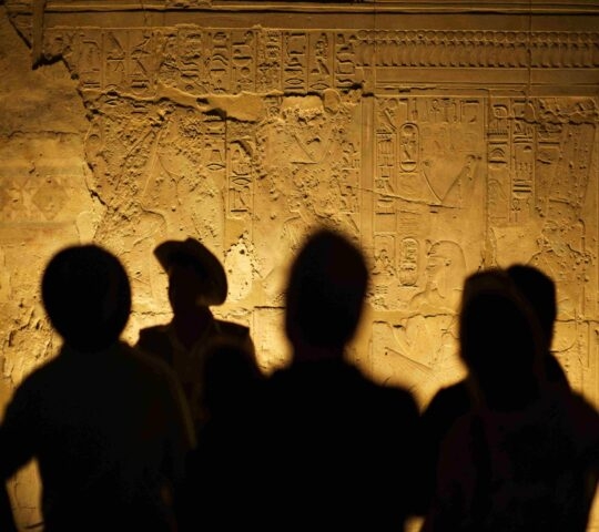 Four human silhouettes on an interior wall of an Egyptian temple covered in hieroglyphics
