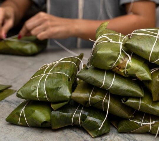 Woman's hands tying a hallaca or tamale in a banana leaf. Traditional food