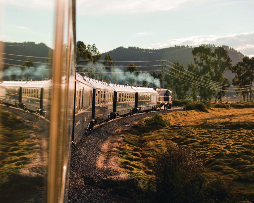Train journey through countryside with smoke trailing and reflection on window.