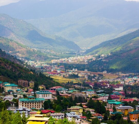 Valley with traditional Bhutanese architecture surrounded by forested hills.