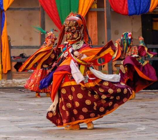 A masked dancer in vibrant, traditional costume performs at a cultural festival.