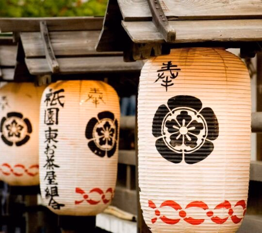 Japanese lanterns with calligraphy and floral patterns hanging from a wooden structure.