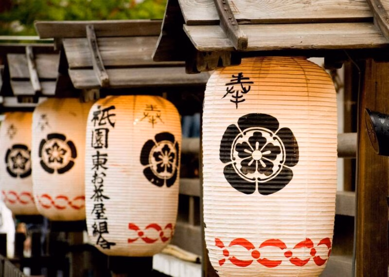 Japanese lanterns with calligraphy and floral patterns hanging from a wooden structure.
