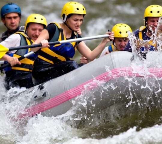 Group of people in helmets and life jackets whitewater rafting.