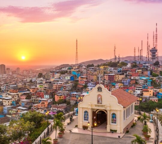 Sunset over a vibrant, colorful hillside cityscape with a small church in the foreground.