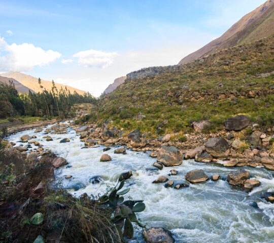 Rushing river with rocks surrounded by mountainous terrain and greenery.