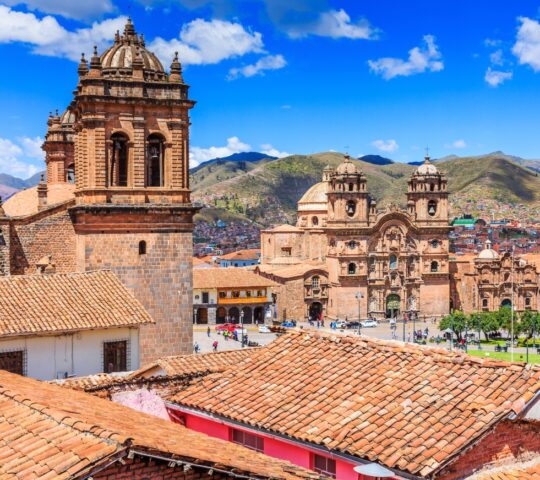 View of historic colonial buildings in Cusco, Peru, with tiled roofs and mountains.