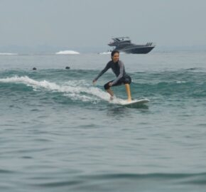 A person surfing on a small wave with a boat in the background on a hazy day.