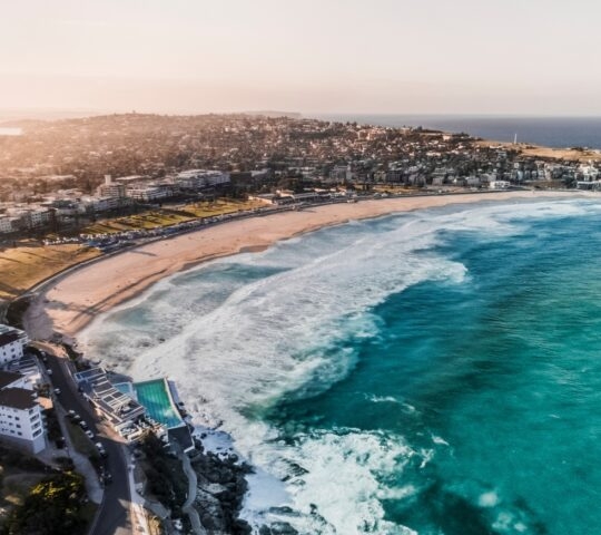 Aerial view of a coastal city with a sandy beach and turquoise sea at sunset.