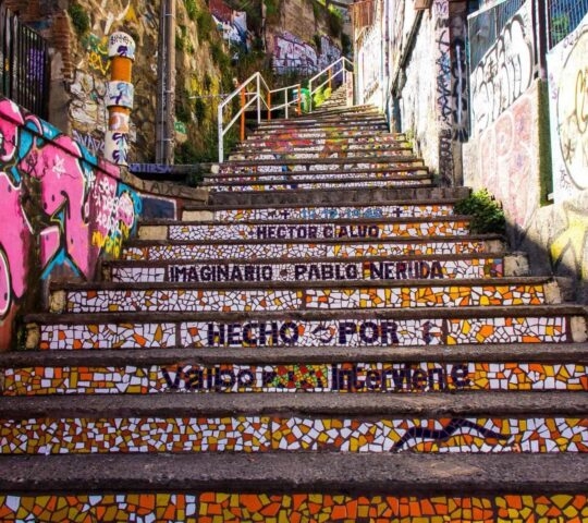 Colorful mosaic stairway with graffiti, inscribed with "Pablo Neruda" among other texts.