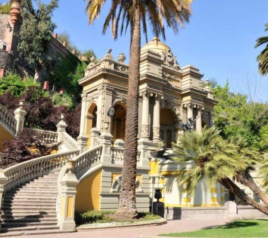 Elegant staircase leading to a historic yellow building with arches and palm trees.