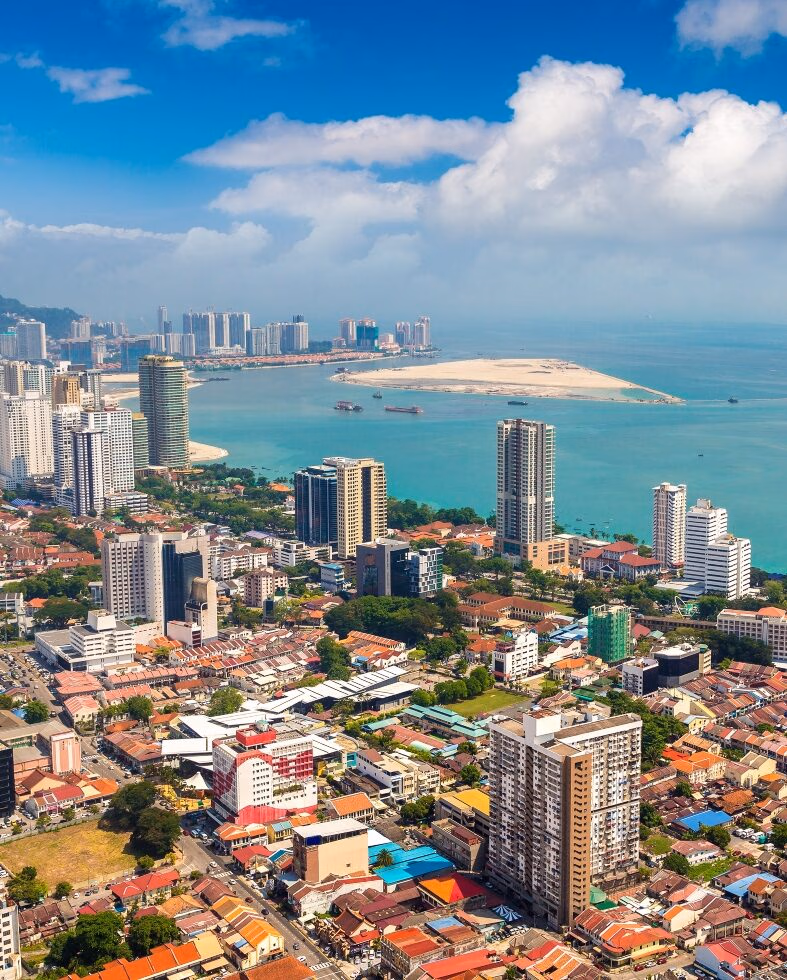 High-rise buildings line the coast of Penang under a blue sky during luxury Malaysia vacations.