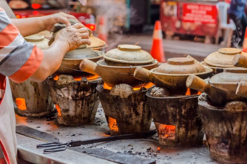 Steam rises from several clay pots cooking over hot coals during luxury Malaysia tours.