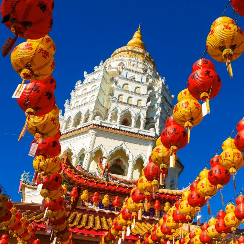 Strands of red and yellow lanterns frame a white multi-tiered pagoda on luxury Malaysia tours.