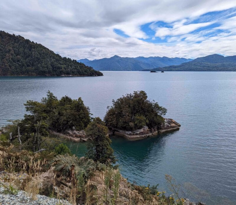 Scenic view of a tranquil blue lake with small green islands and mountainous backdrop.