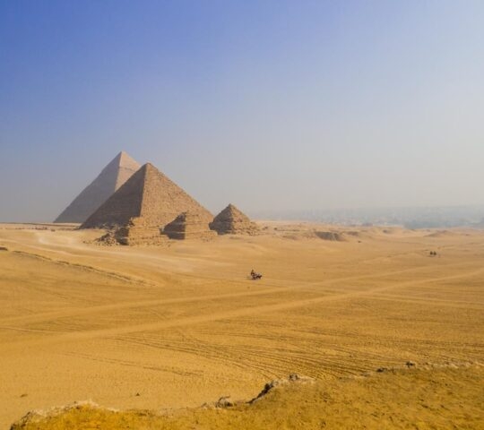 Desert landscape showing the Great Pyramids of Giza under a clear sky.