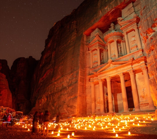 Night view of Al-Khazneh in Petra with candles and starry sky.