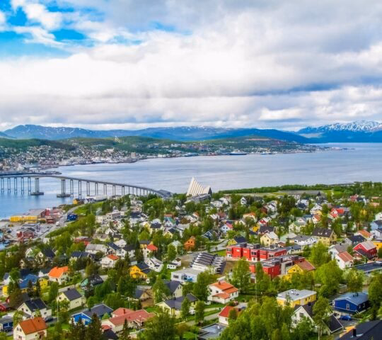 Aerial view of a colorful coastal town with a bridge and mountains in the background.