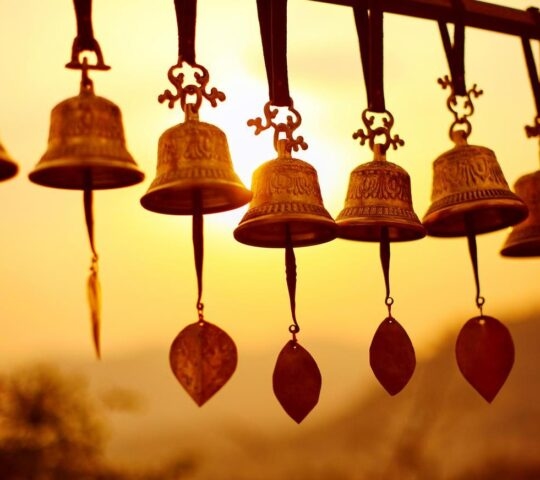 Golden bells with intricate designs hanging against a sunset sky.