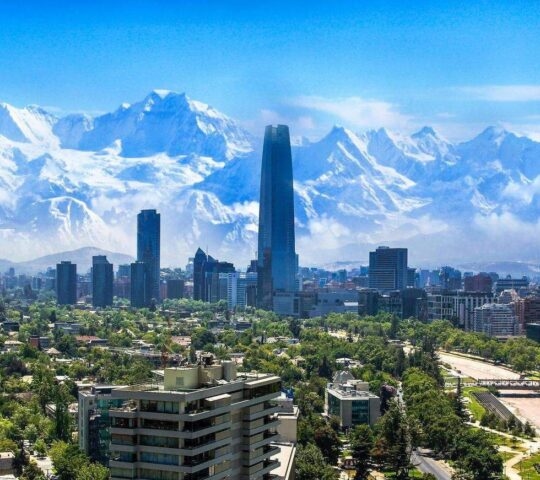 City skyline with modern buildings against a backdrop of snow-capped mountains under a blue sky.