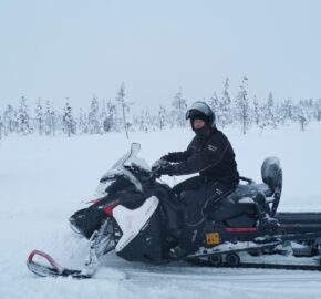 Person riding a snowmobile in a snowy landscape with sparse trees.