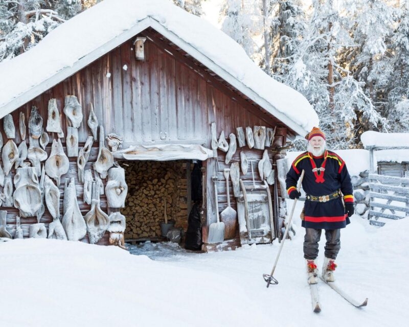 A Sami man stands on skis outside a snow covered lodge in Finnish Lapland