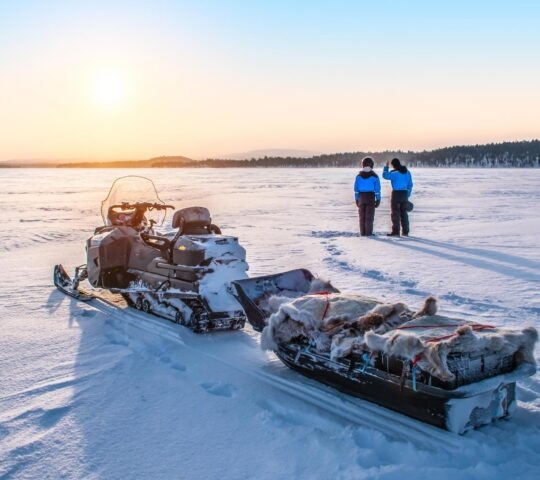 Two people watching sunset with a snowmobile in Finnish Lapland