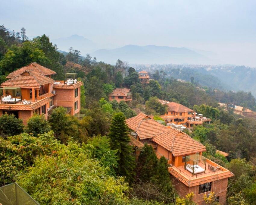 Terracotta-roofed villas on a hilly forest with misty mountains in the background.