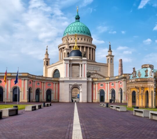 Neoclassical building with a large dome and symmetrical wings under a blue sky.