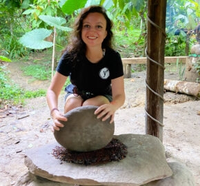 Person in a black shirt grinding something on a stone in a lush green setting.