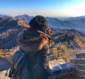 Person gazing at the Great Wall of China winding through mountains at sunset.