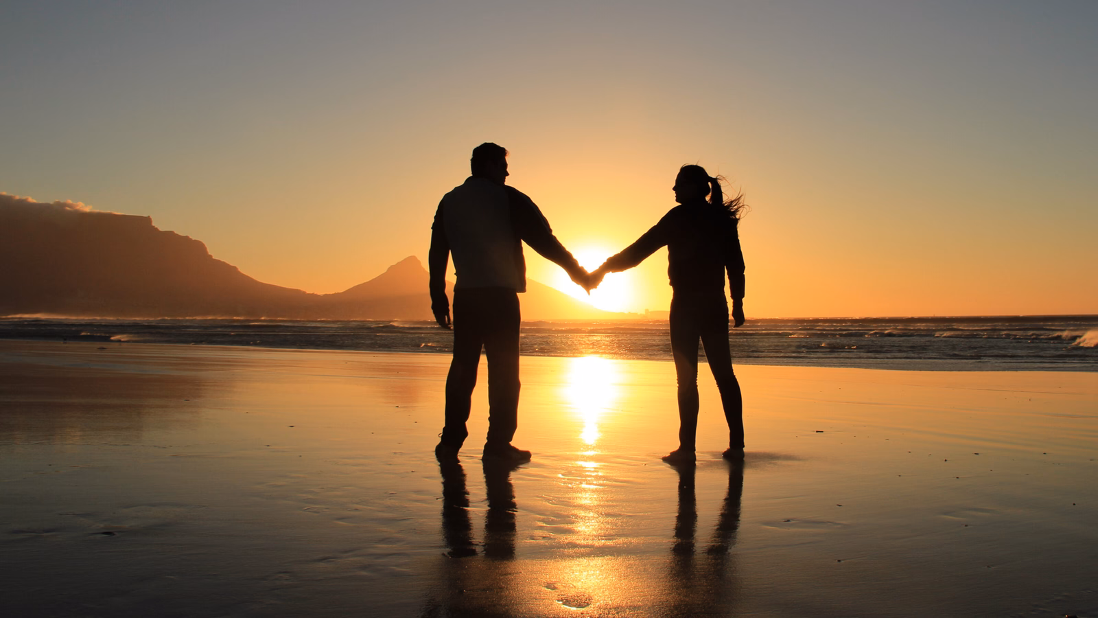 Concept of love and happiness. Silhouette of a romantic couple holding hands on the beach at Cape Town city, South Africa. Man and woman enjoying sunset on beach.