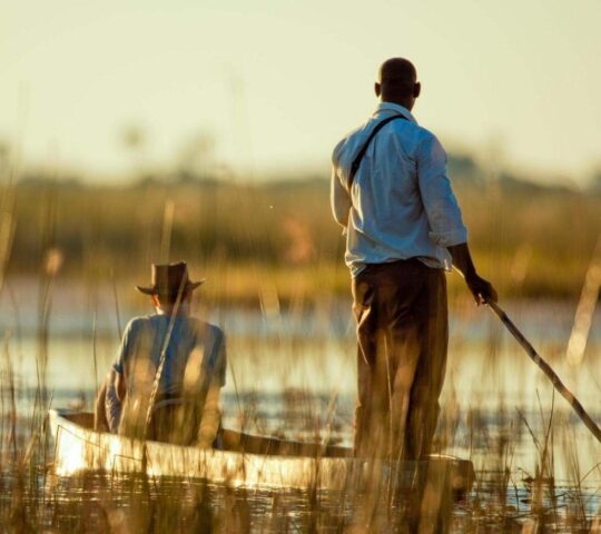 People in a wooden canoe on a calm marshland during Namibia and Botswana Luxury Safaris.
