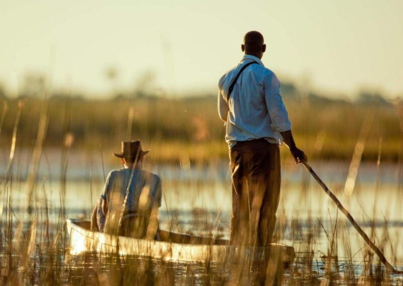 People in a wooden canoe on a calm marshland during Namibia and Botswana Luxury Safaris.