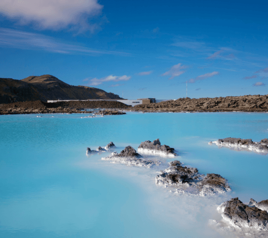Vibrant blue geothermal lagoon with rocky edges under a clear sky.