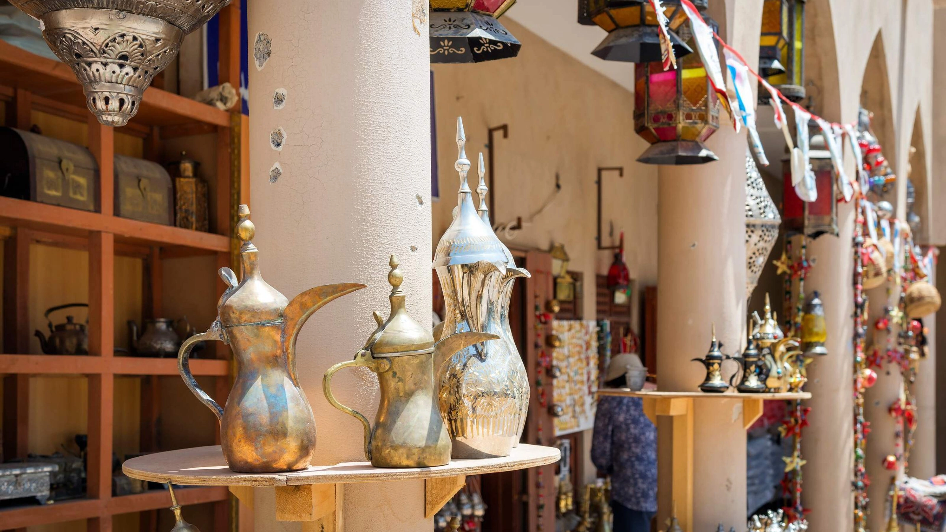 Traditional Middle Eastern metal teapots displayed on a market stand, with colorful lanterns and decorations in the background.