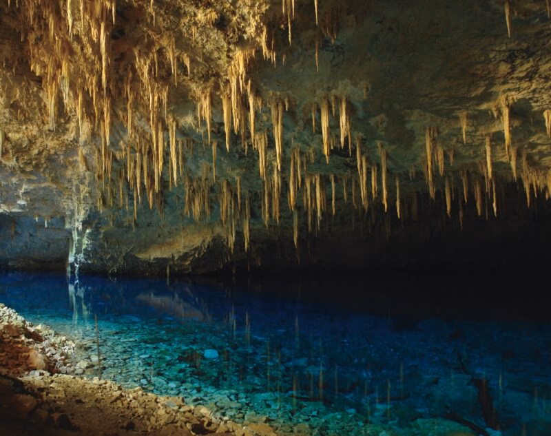 Interior of a cave with many stalactites hanging over clear blue water on luxury Pantanal vacations.