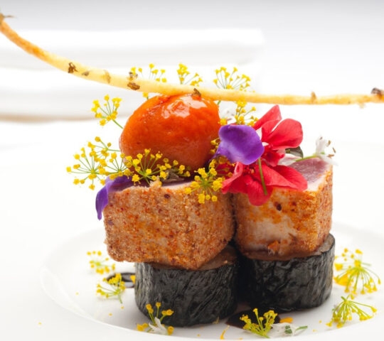 Gourmet dish with seared scallops, vibrant flowers, and a delicate twig.