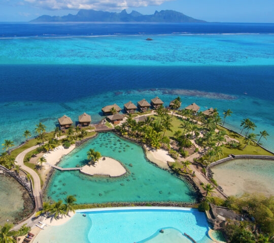 Aerial view of a tropical resort with overwater bungalows and turquoise sea.