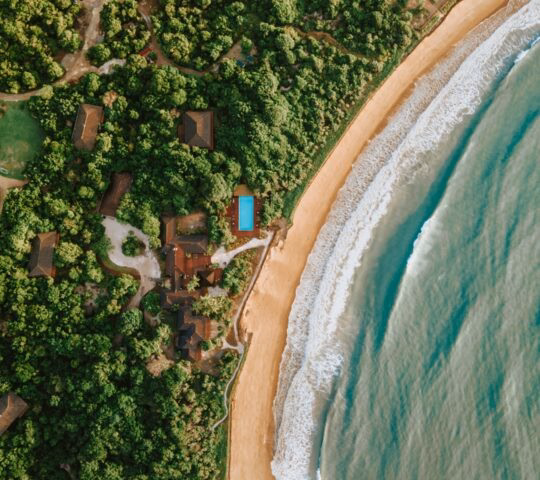 Aerial view of a lush coastal landscape with a sandy beach bordering turquoise ocean waves.