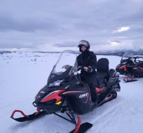Person in a helmet sitting on a snowmobile in a snowy landscape.