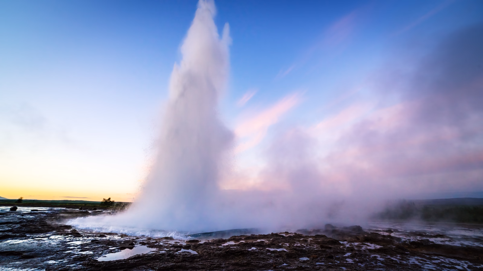 A geyser erupting against a vibrant twilight sky.