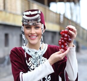Person in traditional attire holding a bunch of grapes.
