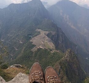 Person's view from a mountaintop overlook, with boots in the foreground and misty Machu Picchu in the distance.