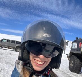 Person in a helmet with a snowy background and vehicles.