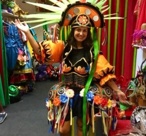 Person in vibrant carnival costume with elaborate headdress and decorated shoulder pieces.