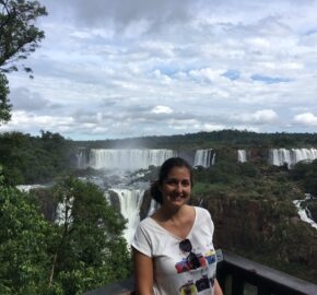 Person in white shirt standing before a panoramic view of majestic waterfalls surrounded by lush greenery.